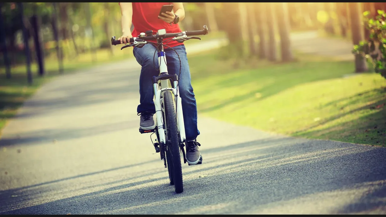 A cyclist holding a smartphone while riding a bicycle on a park path