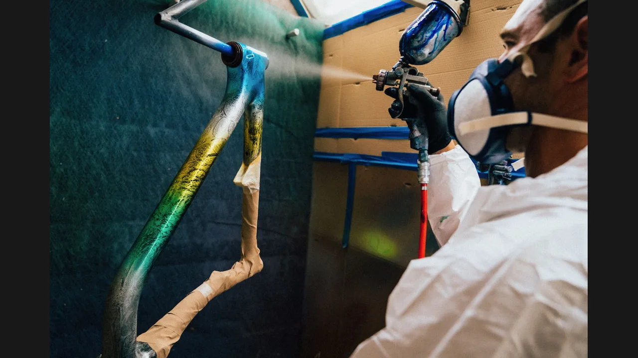 A worker spray-painting a bicycle frame in a workshop